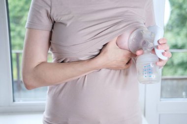 Anne sütünü ifade etmek için elinde makine tutan genç bir kadın. Emzirme kavramı. Göğüs pompası yakın plan.