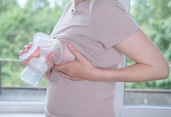 Anne sütünü ifade etmek için elinde makine tutan genç bir kadın. Emzirme kavramı. Göğüs pompası yakın plan.