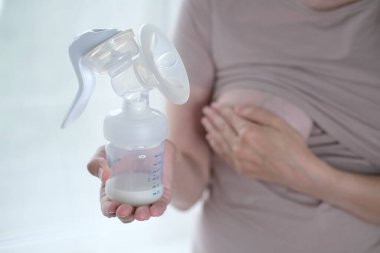 Anne sütünü ifade etmek için elinde makine tutan genç bir kadın. Emzirme kavramı. Göğüs pompası yakın plan.