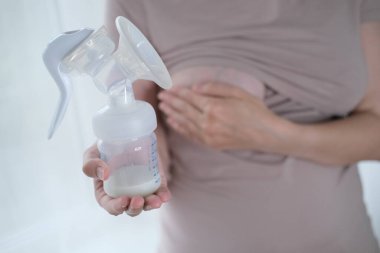 Anne sütünü ifade etmek için elinde makine tutan genç bir kadın. Emzirme kavramı. Göğüs pompası yakın plan.