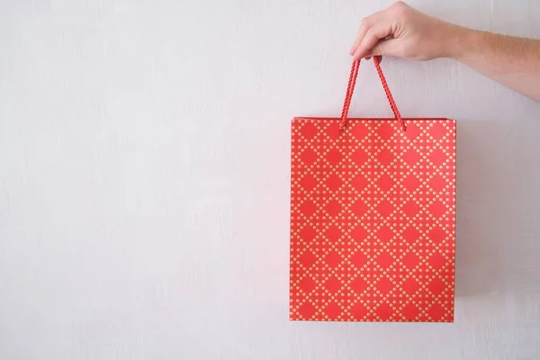 Male hand holds a red gift bag on a white background. A man gives a gift for a holiday.