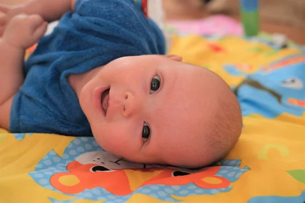 Младенец улыбается. Портрет милого 3-месячного малыша, лежащего на ярком одеяле — стоковое фото