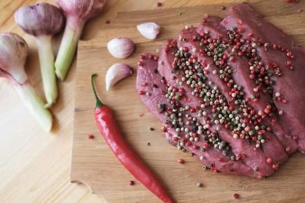 Raw fresh meat is sprinkled with colored peppers and marinated.Grilled beef steak with spices on a wooden cutting board — Stock Photo, Image