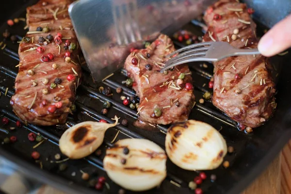 Fried beef or pork steak with onions and peppers lies on a grill pan. The cook cuts the grilled meat of medium rare — Stock Photo, Image