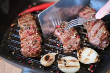 Kızarmış sığır eti ya da soğan ve biberli domuz bifteği ızgarada duruyor. Aşçı orta pişmiş ızgara et keser.