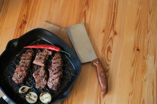 Fried beef or pork steak with onions and peppers lies on a grill pan. The cook cuts the grilled meat of medium rare — Stock Photo, Image