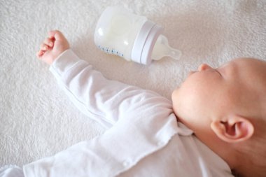 Yeni doğan bebek bir şişeden anne sütü yedi. Beyaz arka planda uyuyan kız ya da erkek.