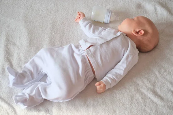 Az újszülött megette az anyatejet egy üvegből. Fiú vagy lány alszik az ágyon fehér háttér — Stock Fotó