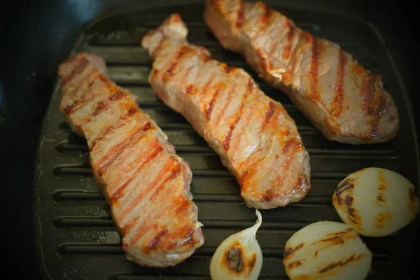 Juicy fried pork or beef with onions lies on the grill pan.Fried meat close-up. — Stock Photo, Image