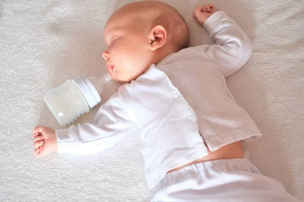 El bebé recién nacido ha comido leche materna de un biberón. Niño o niña durmiendo en la cama sobre fondo blanco — Foto de Stock