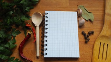 Ahşap kaşık ve baharatların arka planında not defteri olan aşçılık kurulu.