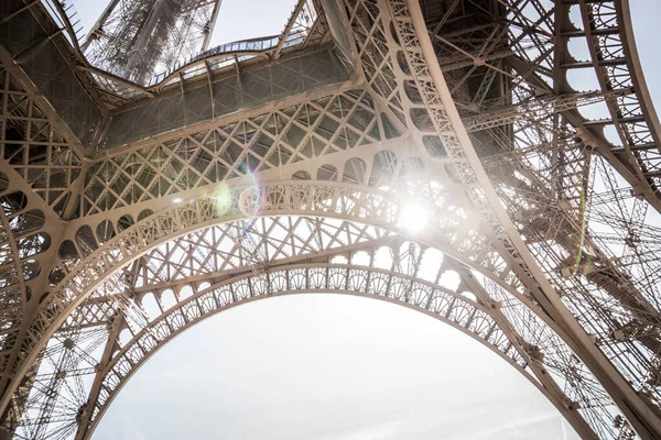 Eiffel Tower in an unusual perspective from below. The rays of the bright sun make their way through the openwork metal structure. A fragment of the Eiffel Tower. Paris, France. Travel concept.