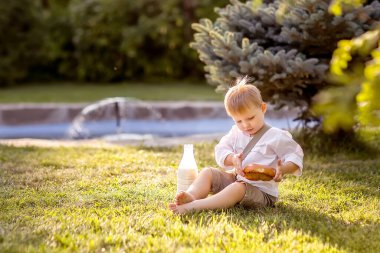 Küçük bir çocuk mavi bir ladin yakınında çimlerin üzerinde oturuyor. Çocuğun bir şişe sütü ve ev yapımı ekmeği var. Çocuk çörek yiyor. Doğa yürüyüşü.
