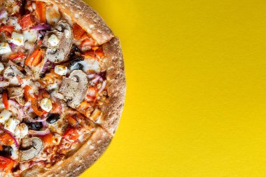 Sebzeli yarım pizza parlak sarı bir arka plandadır. Mesaj için yer var. Yukarıdan görünüşü.