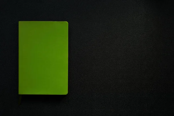Siyah deri arka planda yeşil defter. Defter sol köşede..