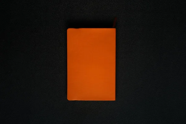 Siyah deri arka planda turuncu defter. Defter ortada.