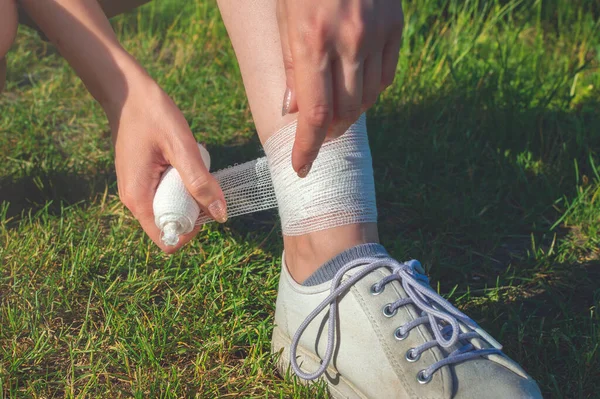 Close-up scene. Young woman runner outdoors puts a bandage on her injured leg on her own. — Stock Photo, Image