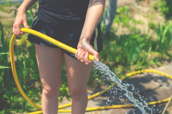 Taman musim panas, berair. Slim wanita muda bercelana pendek bersenang-senang di kebun dengan selang taman memercikkan hujan. Close-up — Stok Foto