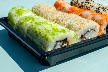Taze Japon dürümleri ve balıklarla dolu bir set. Konforlu ambalajda yiyecek. Paket servis için suşi ya da plastik kabın içinde suşi servisi. Bir açıyla kenar görünümü.