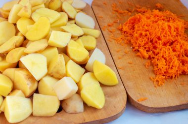 Bir sürü dilimlenmiş patates ve rendelenmiş havuç mutfakta yemek pişirirken tahta kesiyor..