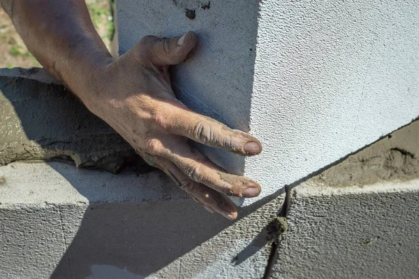 Bir inşaatçının kirli erkek elleri bir duvar inşa ederken bir köpük bloğu yükler