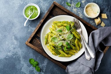 Penne rigate makarna parmesan peyniri ve fesleğen ile seramik tabak içinde gri vintage eski beton arka plan üzerinde bırakır. Seçici odak.