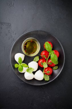 Kiraz domates, fesleğen, mozzarella peyniri ve zeytinyağı koyu arka plan üzerinde siyah plaka. İtalyan yemeği arka plan. Seçici odak. Üstten görünüm.