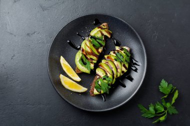 Avokado, limon ve siyah beton eski arka plan üzerine Balsamik sosu baharatlı çavdar tost. Seçici odak. Üstten görünüm.