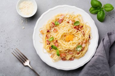 Makarna spagetti carbonara pastırma, kaşar peyniri, yumurta sarısı ve fesleğen ile ışık gri arka plan üzerinde bırakır. Geleneksel İtalyan yemeği. Üstten görünüm.