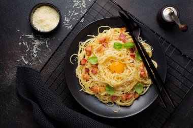 Makarna spagetti carbonara pastırma, kaşar peyniri, yumurta sarısı ve fesleğen ile siyah arka plan üzerine bırakır. Geleneksel İtalyan yemeği. Üstten görünüm.