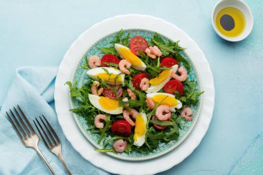 Roka, salatalık, domates, yumurta ve karides salatası soya sosu seramik plaka üzerinde. Seçici odak. Üstten görünüm.