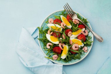 Roka, salatalık, domates, yumurta ve karides salatası soya sosu seramik plaka üzerinde. Seçici odak. Üstten görünüm.