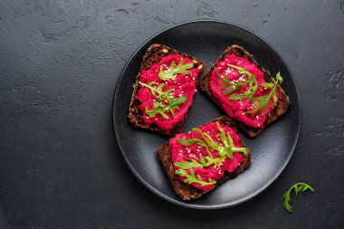 Bruschetta karanlık beton zemin üzerine kırmızı pancar Humus, roka ve susam tohumu ile. Üstten görünüm.