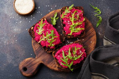 Bruschetta karanlık beton zemin üzerine kırmızı pancar Humus, roka ve susam tohumu ile. Üstten görünüm.