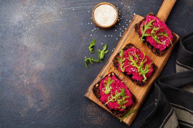 Bruschetta karanlık beton zemin üzerine kırmızı pancar Humus, roka ve susam tohumu ile. Üstten görünüm.