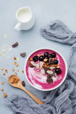Pembe siyah frenk üzümü çilek, muz smoothie kaseyle granola, badem ve çikolata ışık gri beton zemin üzerine pul. Seçici odak. Üstten görünüm. Kopya alanı.