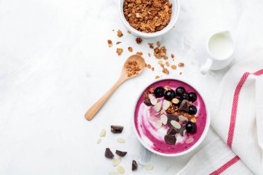 Pembe siyah frenk üzümü çilek, muz smoothie kaseyle granola, badem ve çikolata ışık gri beton zemin üzerine pul. Seçici odak. Üstten görünüm. Kopya alanı.