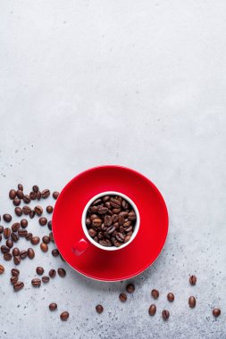 Kahve çekirdekleri içinde gri beton zemin üzerine kırmızı fincanla. Üstten görünüm.