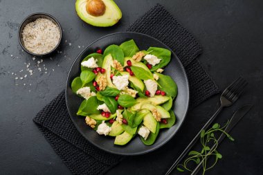 Taze yararlı vejetaryen sağlıklı avokado, ıspanak, nar taneleri, ceviz, safran, biber ve ricotta Salata siyah arka plan üzerine. Seçici odak. Üstten Görünüm. Metin için yer kopyalayın.
