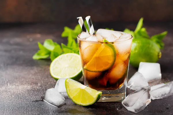 Summer cooling alcoholic beverage from cola, whiskey, lime and liqueur in glass on dark concrete old background.