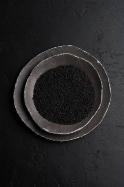 Siyah susam karanlık eski antika arka plan üzerinde siyah seramik tabak içinde. Rustik tarzı. Üstten görünüm.