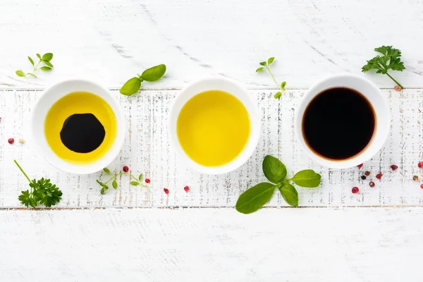 Soy sauce, olive oil and balsamic sauce with herbs basil, parsley, pepper and thyme on white wooden background. Top view.