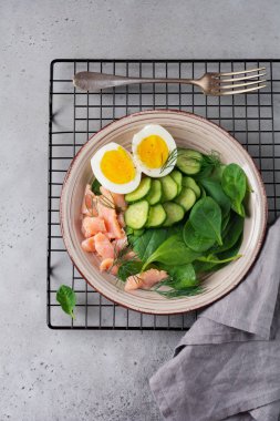 Pembe somon füme, ıspanak, salatalık ve tavuk yumurta gri seramik tabak İskandinav salatası. Üstten görünüm. 