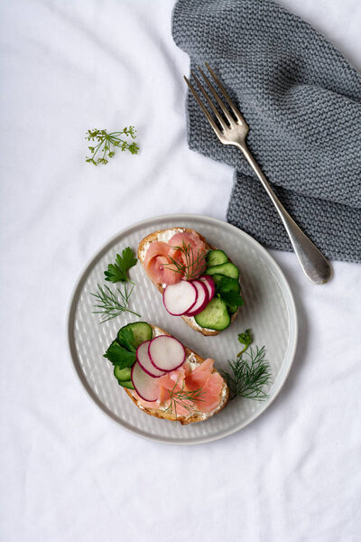 Сэндвичи с копченым розовым лососем, редькой, огурцом и сливочным сыром на серой керамической тарелке и текстильном фоне. Традиционные скандинавские тосты. Вид сверху
.