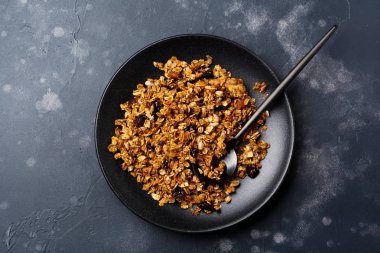 Yulaf ezmesi granola koyu arka plan üzerinde siyah seramik tabak içinde kuru meyve, chia tohum ve ayçiçeği, tatlım. Üstten görünüm.