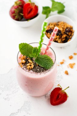 Pembe çilek, muz smoothie granola ve chia tohumu hafif beyaz beton zemin üzerine cam ile. Üstten görünüm. Kopya alanı.