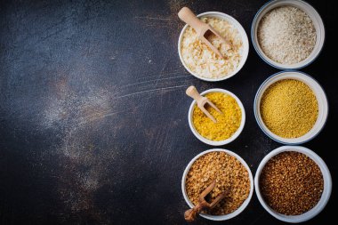 Çeşitli tahıl gevreği pirinç, darı, buğday, yulaf ezmesi. Superfood karanlık eski beton zemin üzerine beyaz seramik kase. Üstten görünüm.