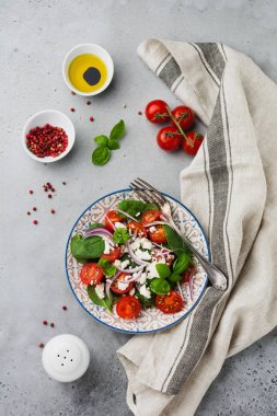 Domates, ıspanak yaprakları, kırmızı soğan ve beyaz peynirli salata gri artalanları üzerinde ışık seramik plaka üzerinde. Seçici odak. Üstten görünüm.