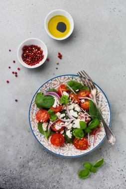 Domates, ıspanak yaprakları, kırmızı soğan ve beyaz peynirli salata gri artalanları üzerinde ışık seramik plaka üzerinde. Seçici odak. Üstten görünüm.