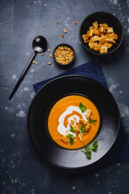 Kabak Koyu ahşap arka plan üzerinde siyah seramik tabak içinde fındık kremalı ekmek ve sedir çorba. Geleneksel sonbahar gıda. Üstten görünüm kopya alanı.